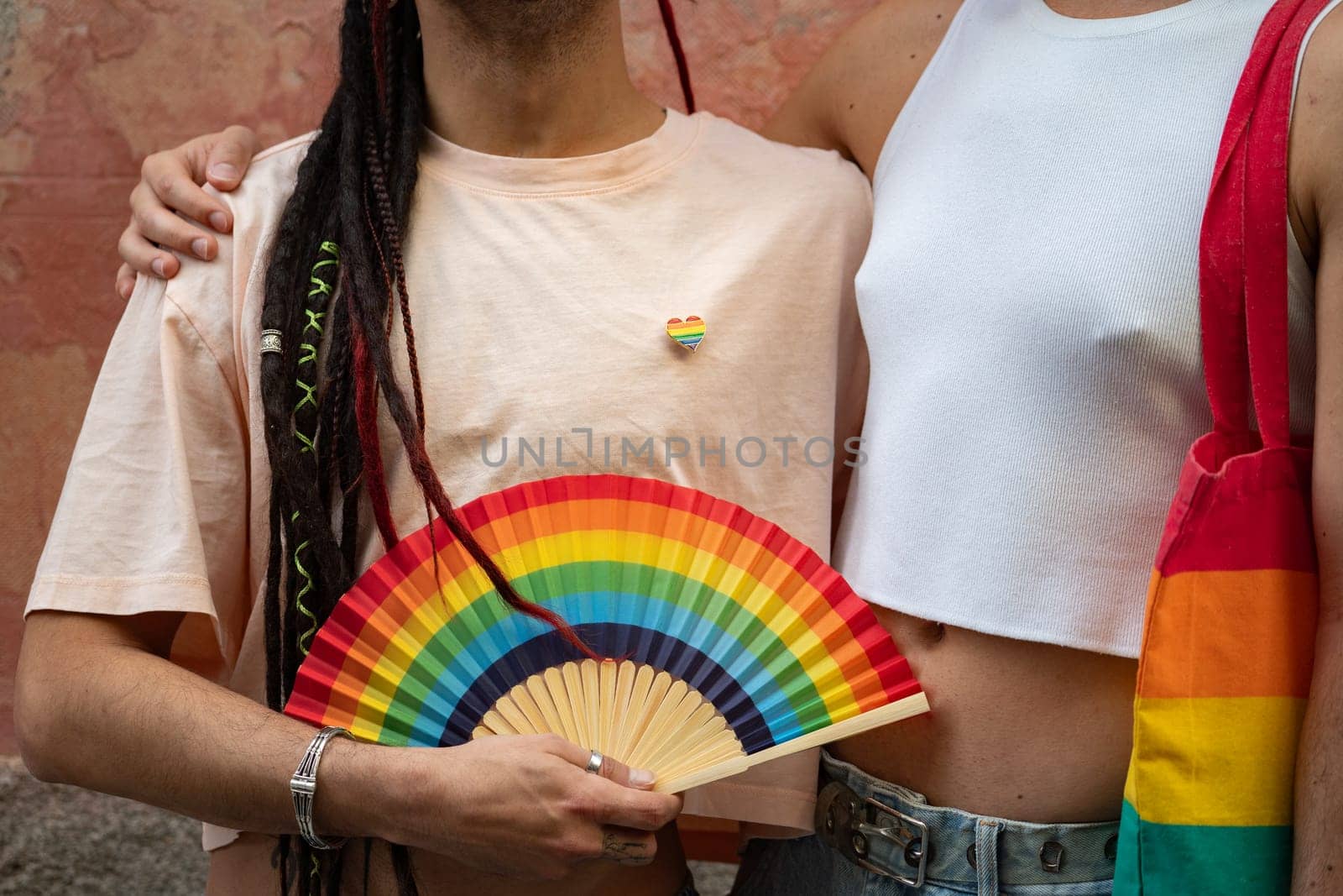 Unrecognizable close up photo of men couple holding rainbow fan , bag and pin to support LGBTQ community.