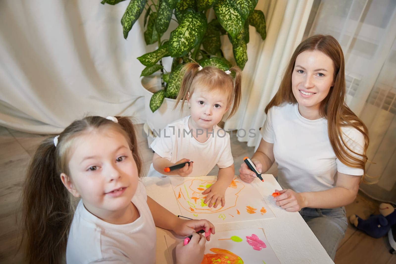 Young mother or babysitter, little daughter, sister teenager girl drawing at table in room. Painting, doing homework. Family enjoying leisure at home
