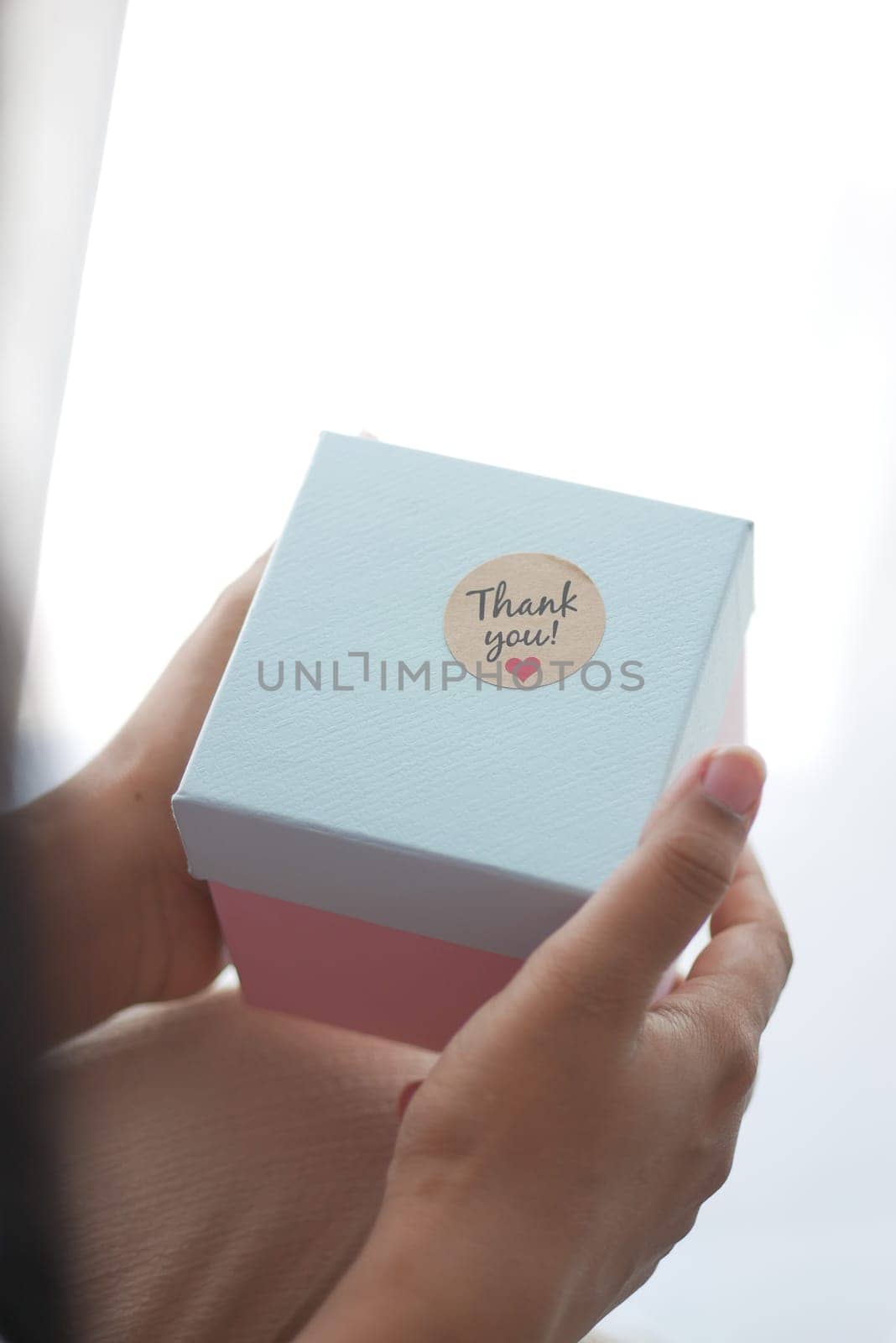 hand putting a thank you sticker on a gift box .