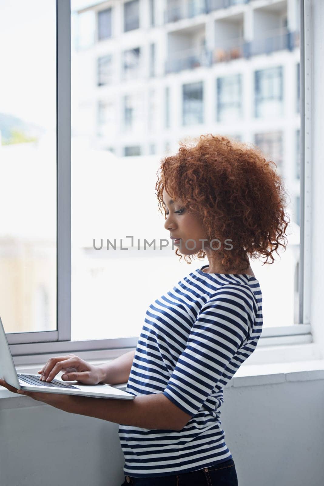 Office, window and black woman typing on laptop with research or online communication on email. Creative, employee and working with computer to scroll information or news on internet for business.