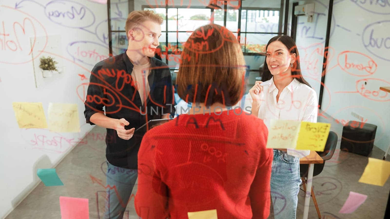 Creative start up team brainstorming marketing idea while cooperative caucasian businesswoman presents creative solution in front of glass board at business meeting. Working together. Immaculate.