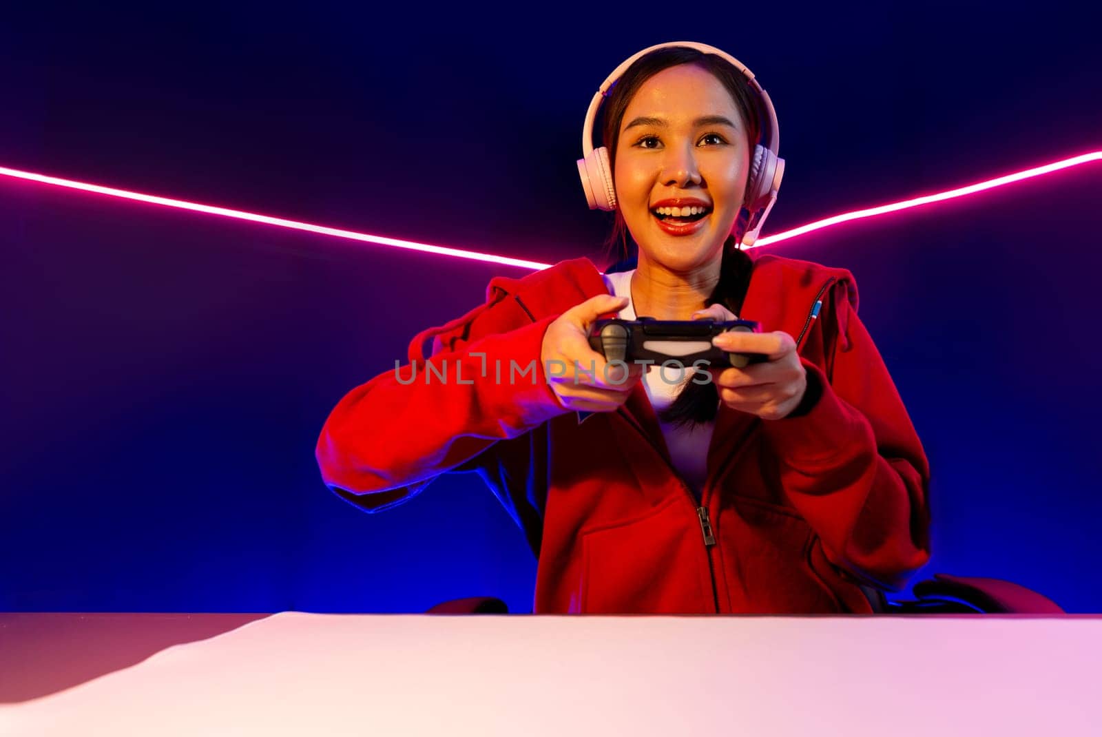 Host channel of smiling beautiful Asian girl streamer with joystick playing online game wearing headphones paste talking with viewers media online. Esport skilled team players in neon room. Stratagem.