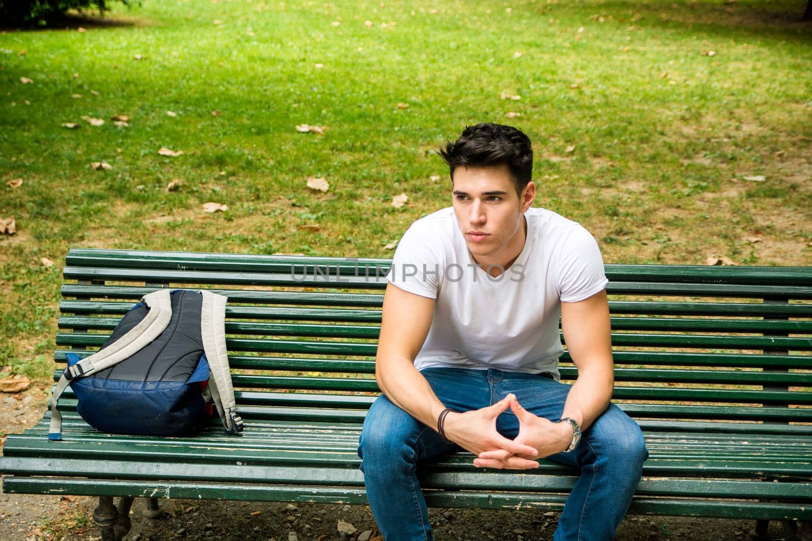 A man sitting on a bench with a back pack. Photo of a man sitting on a bench with a backpack