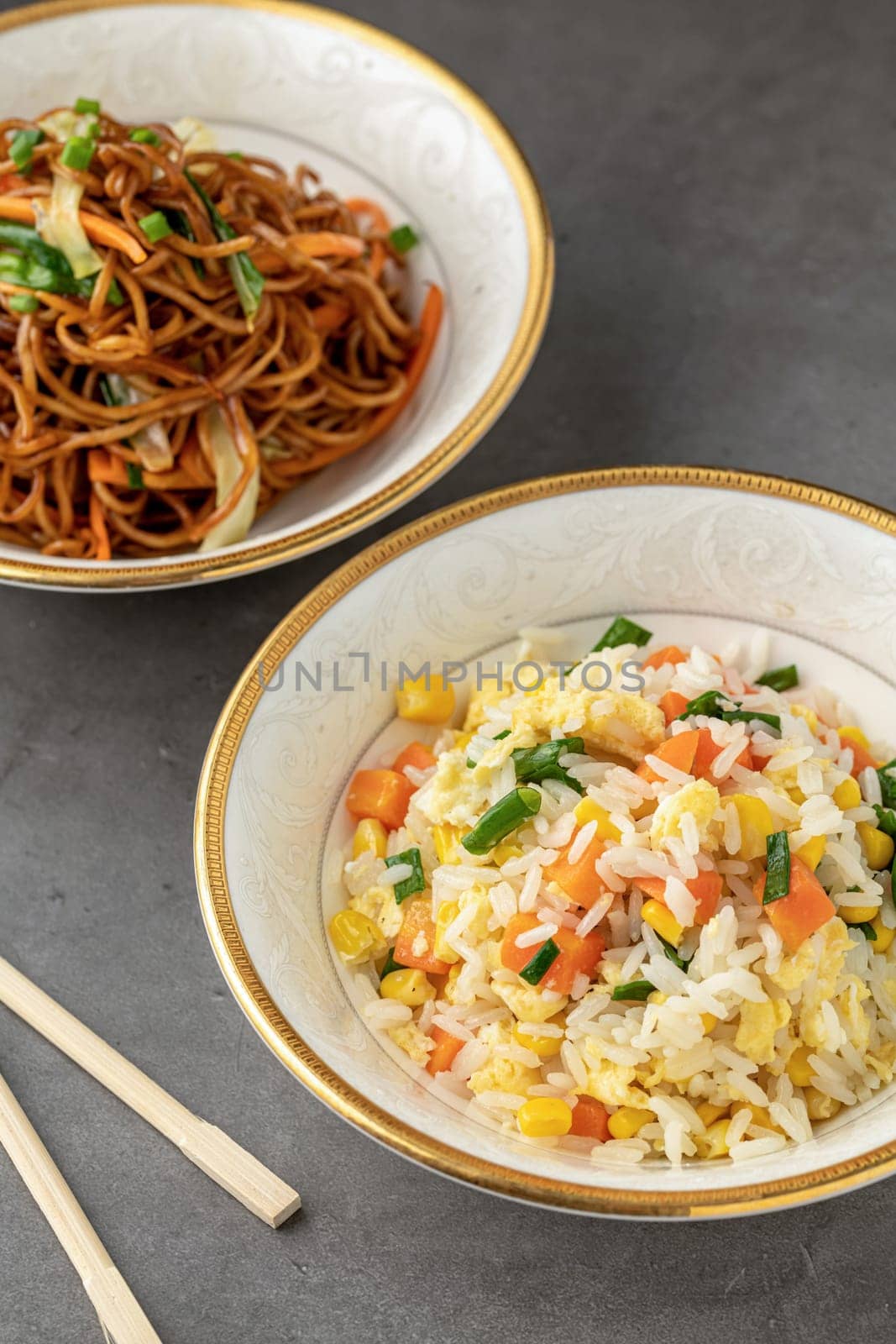 Noodles with vegetables and rice pilaf with egg and corn in a white bowl on a dark background by Sonat