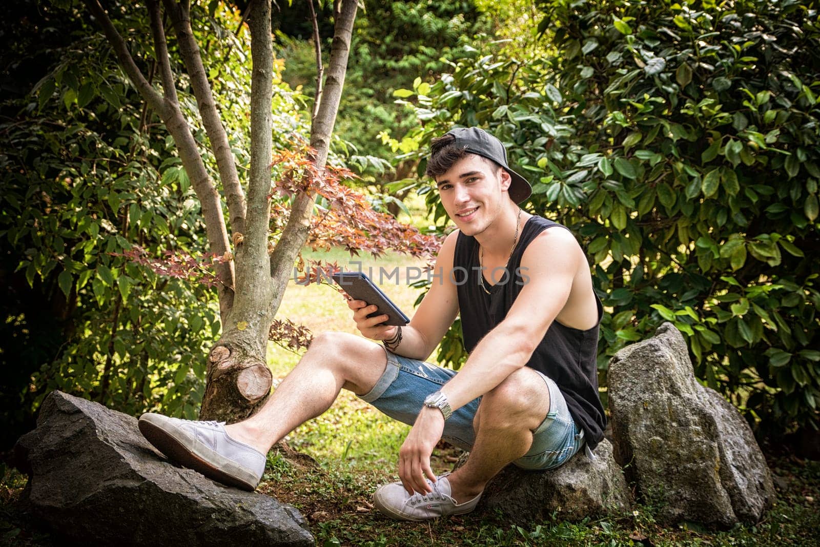 A man sitting on a rock looking at a tablet. Photo of a man sitting on a rock engrossed in his ebook reader