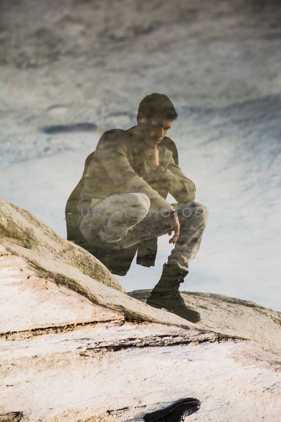 A man sitting on top of a rock next to the ocean. Photo of a man enjoying the scenic view of the ocean from atop a majestic rock