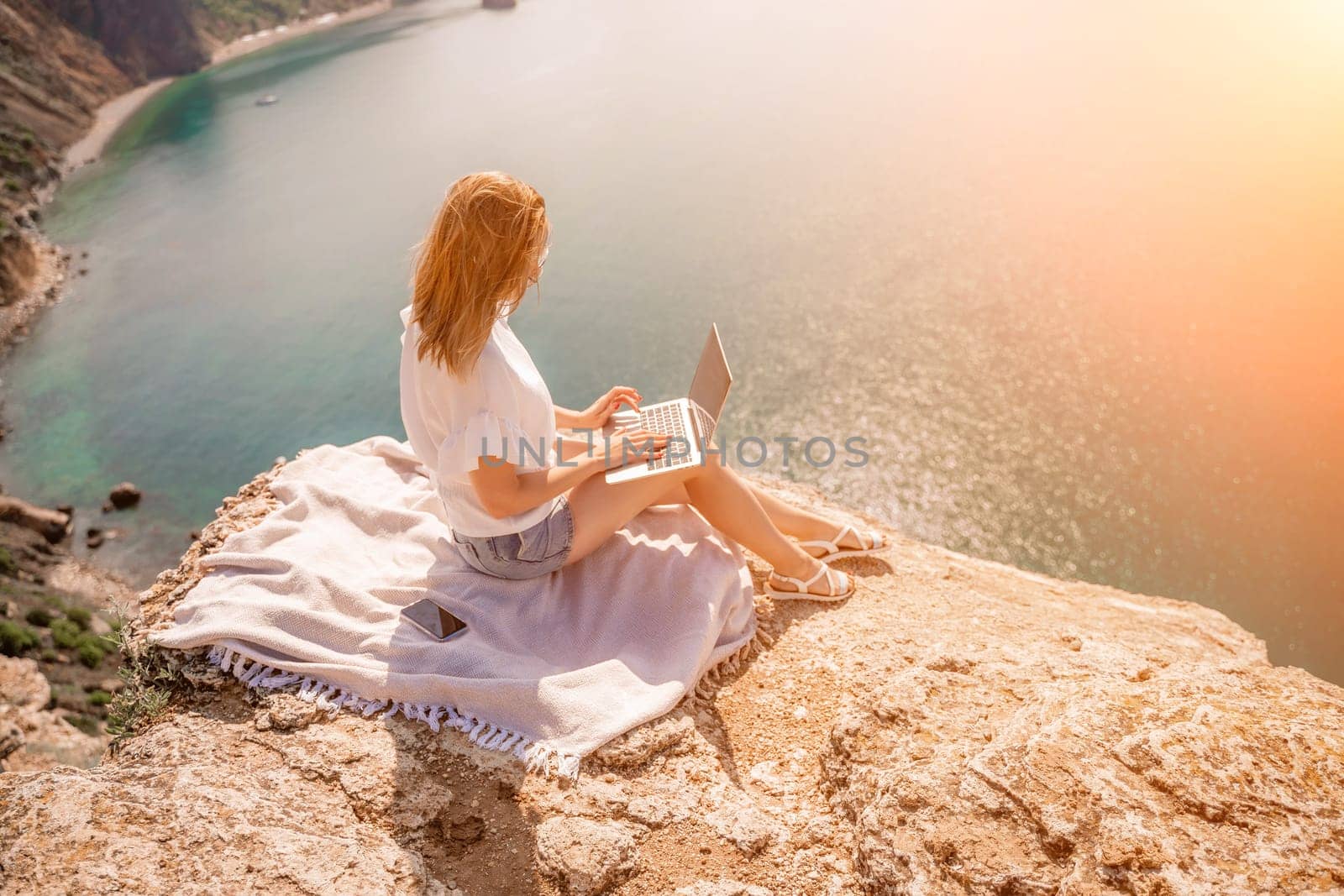 Freelance woman working on a laptop by the sea, typing away on the keyboard while enjoying the beautiful view, highlighting the idea of remote work