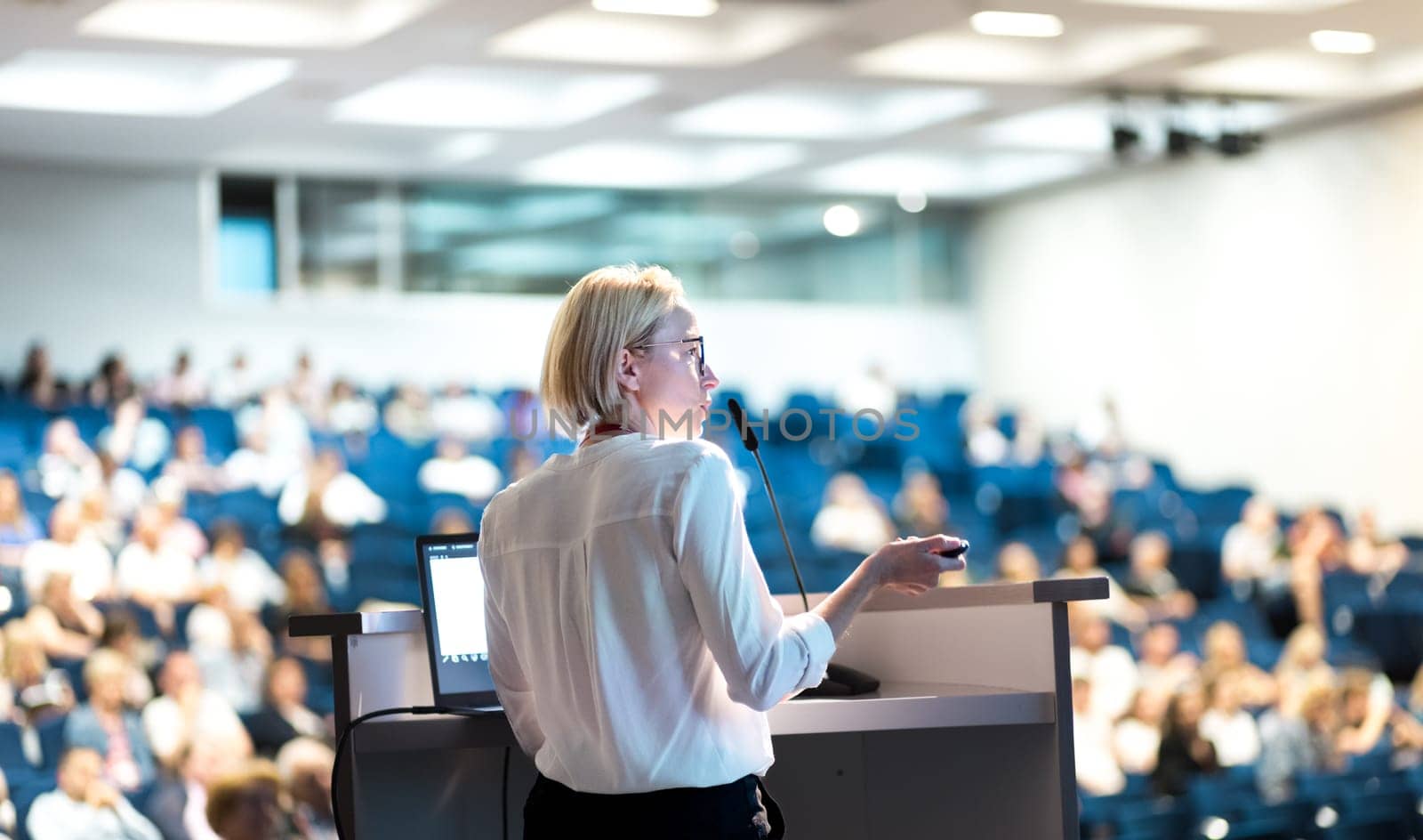 Female speaker giving a talk on corporate business conference. Unrecognizable people in audience at conference hall. Business and Entrepreneurship event. by kasto