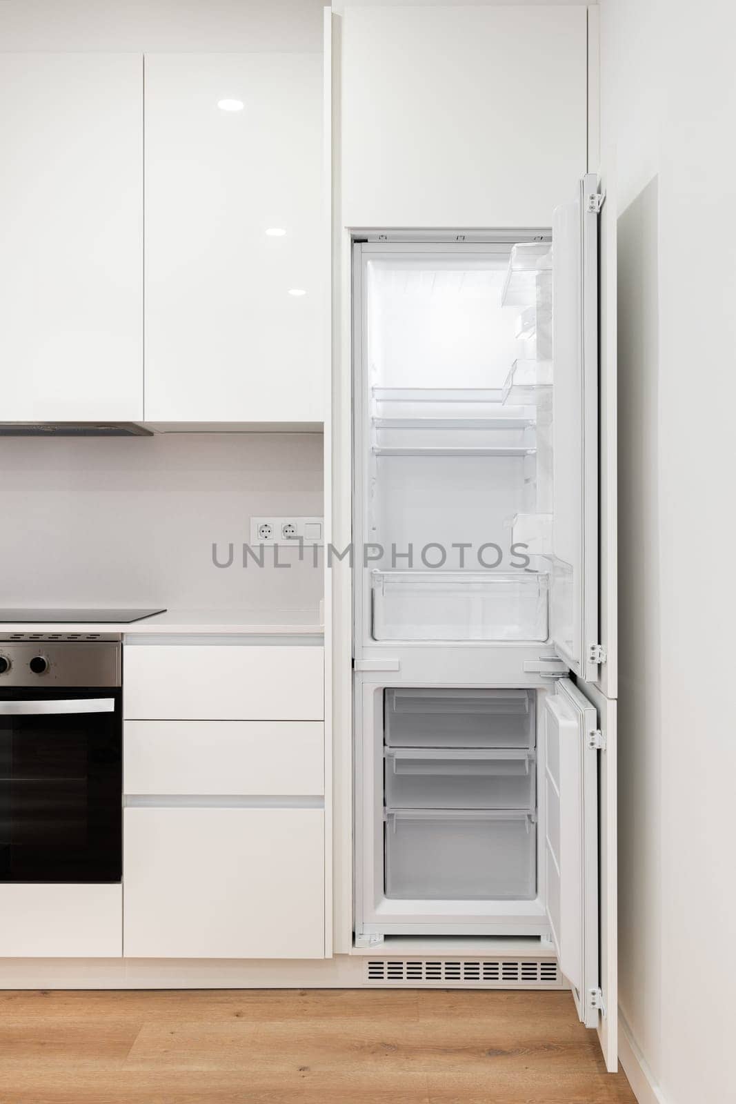 Photo of a modern kitchen with sleek white cabinets and empty refrigerator and freezer with doors open.