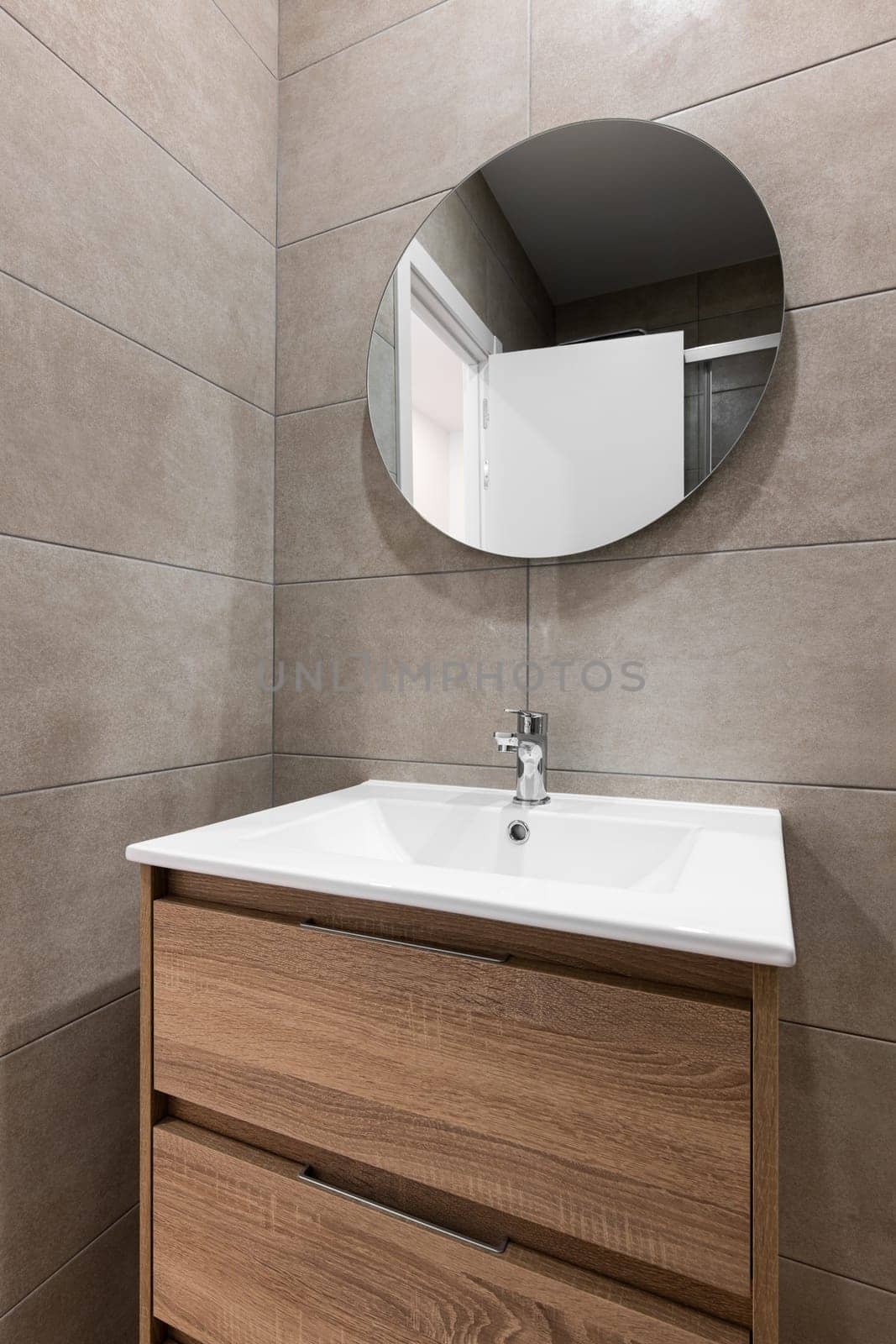 Modern bathroom with a sleek sink, wooden furniture and a round mirror.