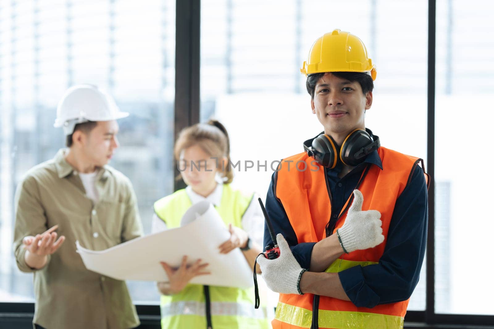 Portrait of civil engineer with hard hat holding radio walkie talkie while supervisor engineers and architect planning in background by itchaznong