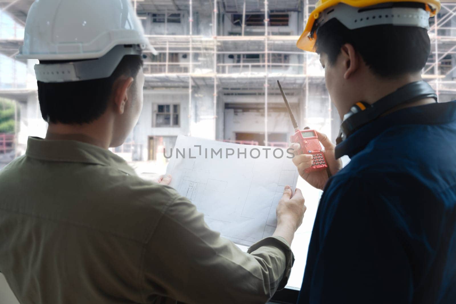 Civil engineers and architects inspecting and working building site with blueprints and holding walkie talkie.