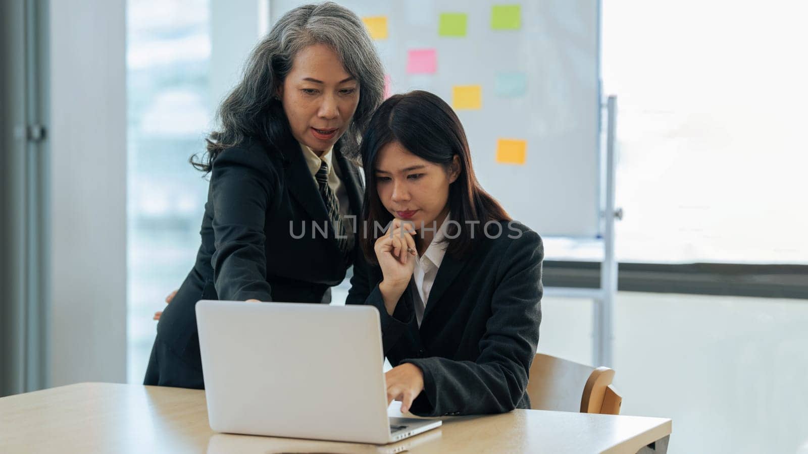 young financial assistant working on laptop while senior professional standing and giving investment advise.