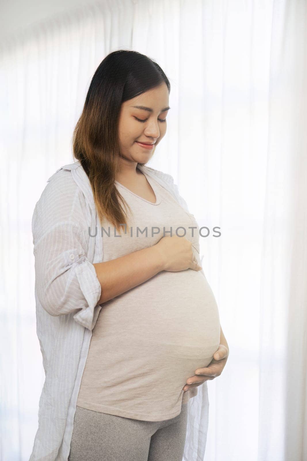 pregnancy woman hugging her tummy and feel happy with big belly at window by itchaznong