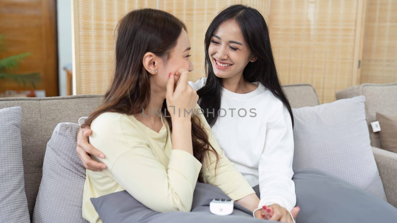 Loving LGBTQIA lesbian gay couple laughing together in Livingroom. Asian LGBTQIA lesbian gay couple laughed happy together while sitting on the sofa. Homosexual-LGBTQ concept..