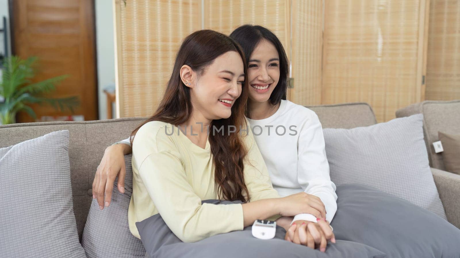 Loving LGBTQIA lesbian gay couple laughing together in Livingroom. Asian LGBTQIA lesbian gay couple laughed happy together while sitting on the sofa. Homosexual-LGBTQ concept..