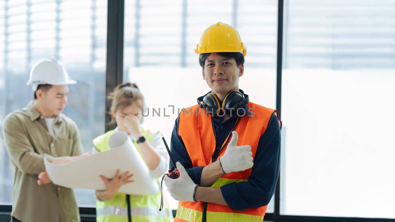 Portrait of civil engineer with hard hat holding radio walkie talkie while civil engineer planning in background.