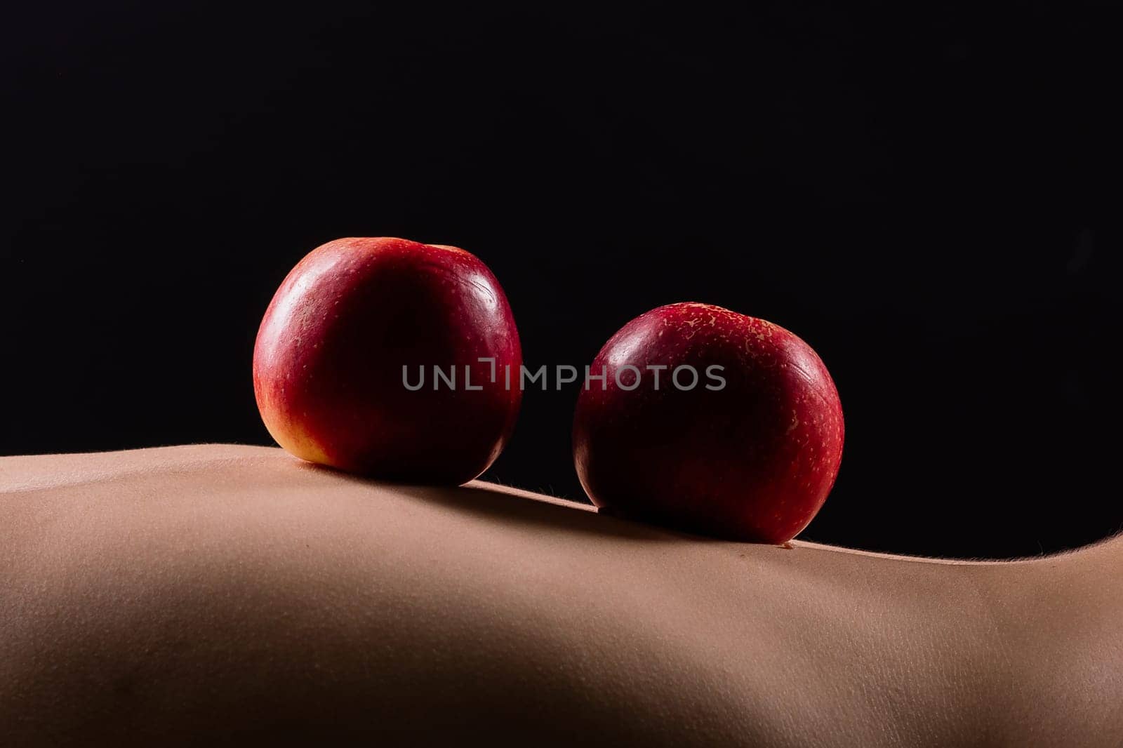 Nude woman with red apple on her back, dark background by Zelenin