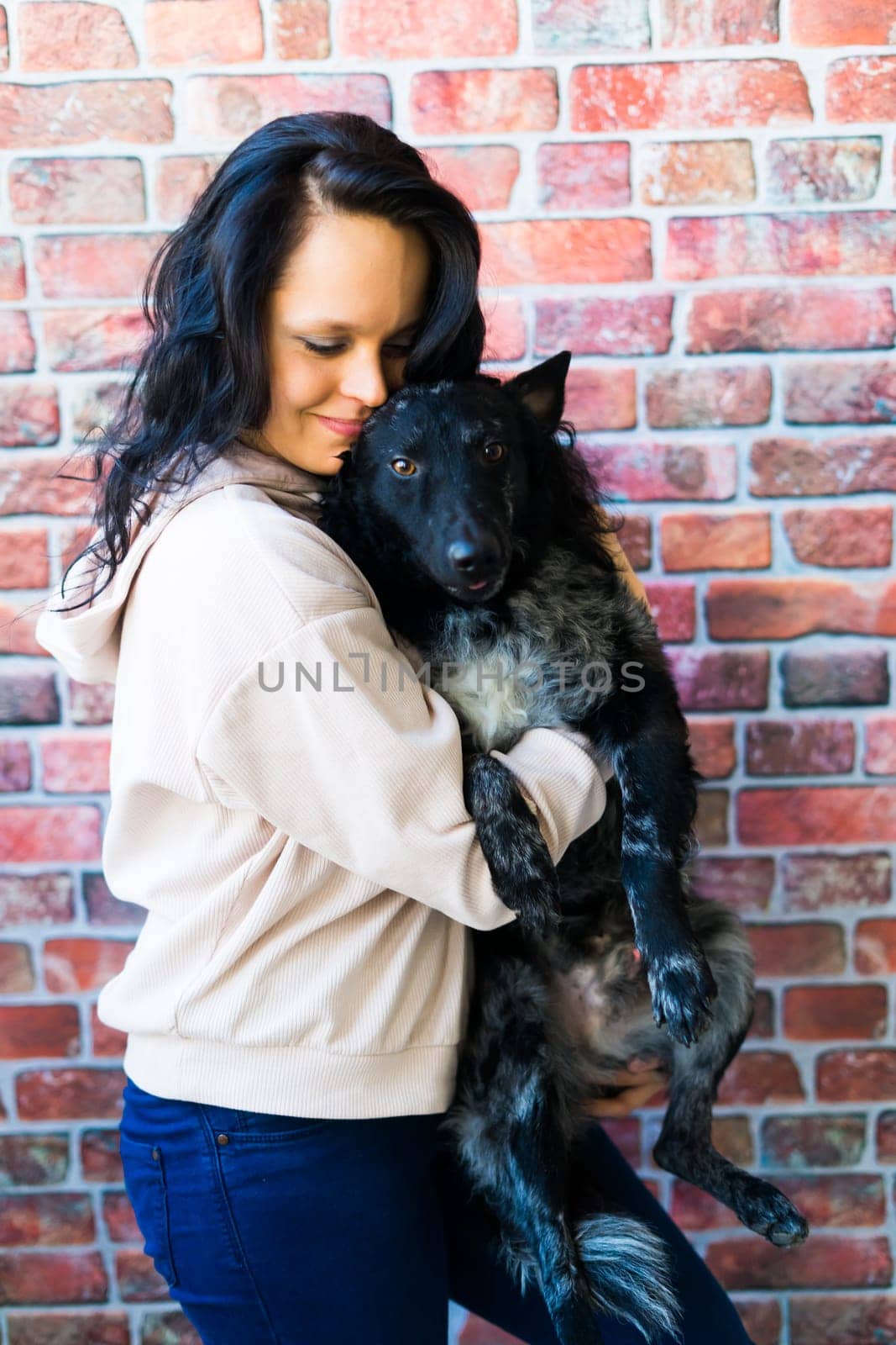 Happy brunette lady in casual wear hugging mudi pet dog, studio background. by Zelenin