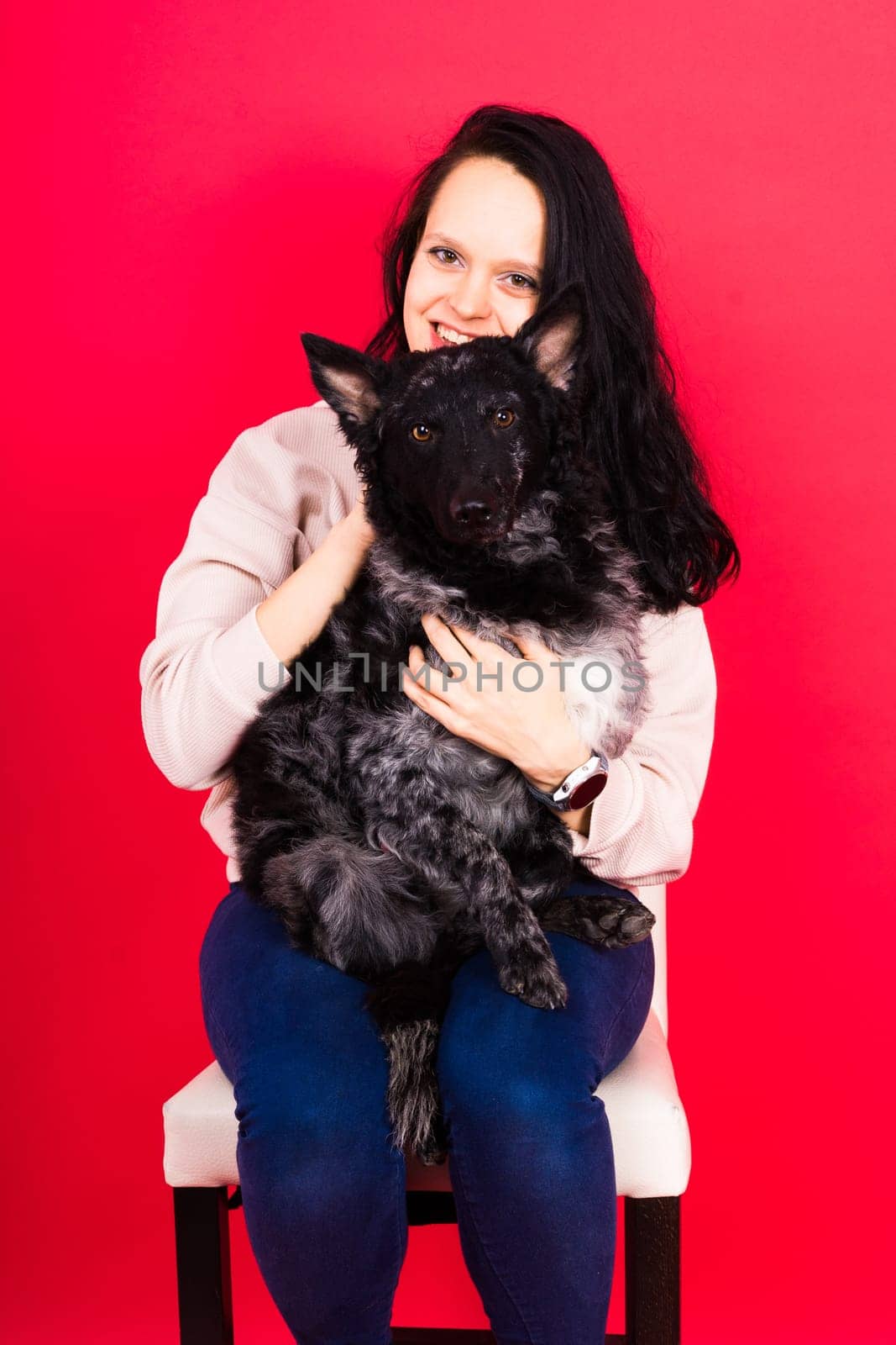 Happy brunette lady in a casual wear hugging mudi pet dog, studio background.