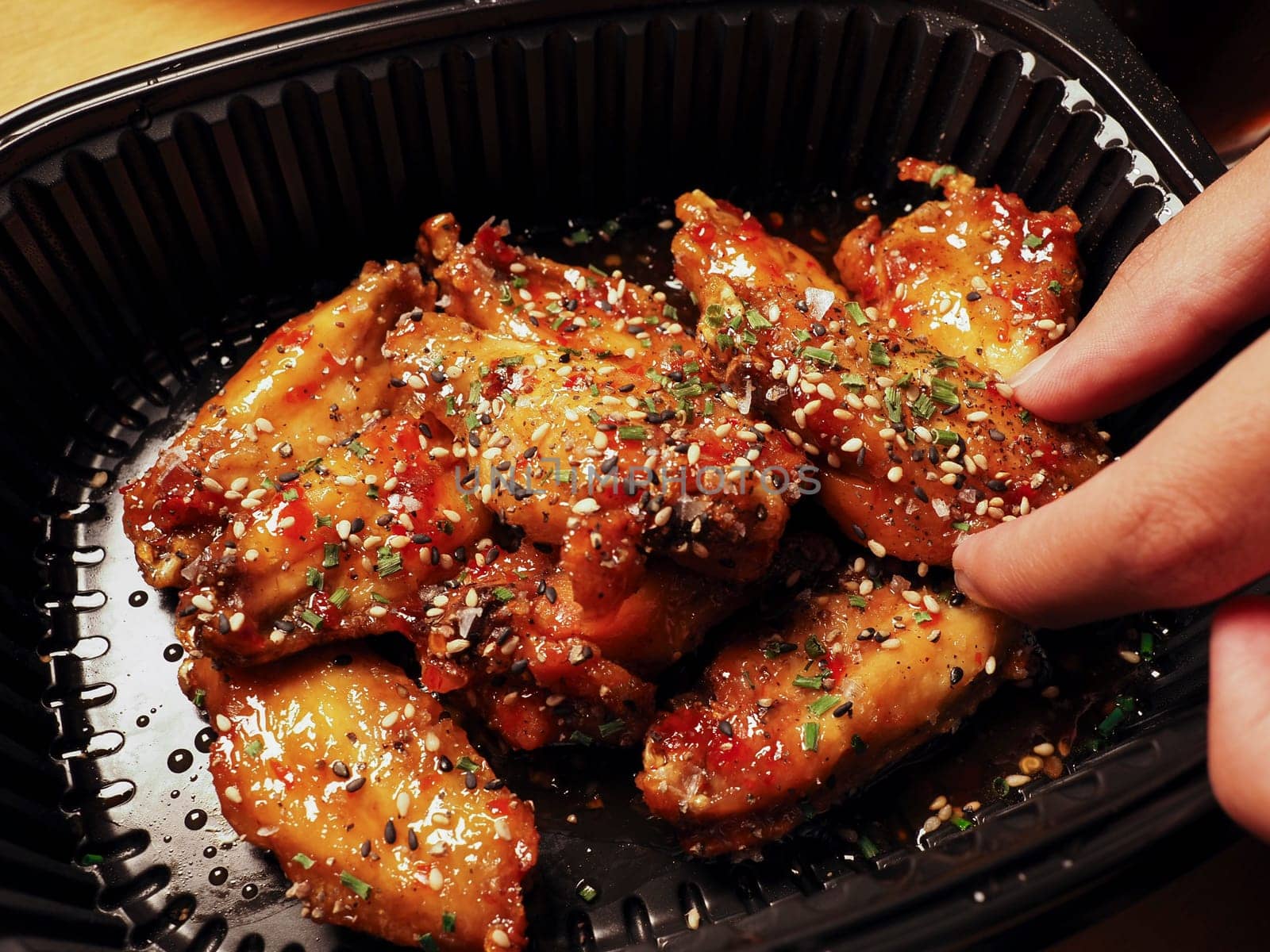 Man's hand picking up a Korean Chicken wings with sauce. 치킨. Asian street food. Delivery concept