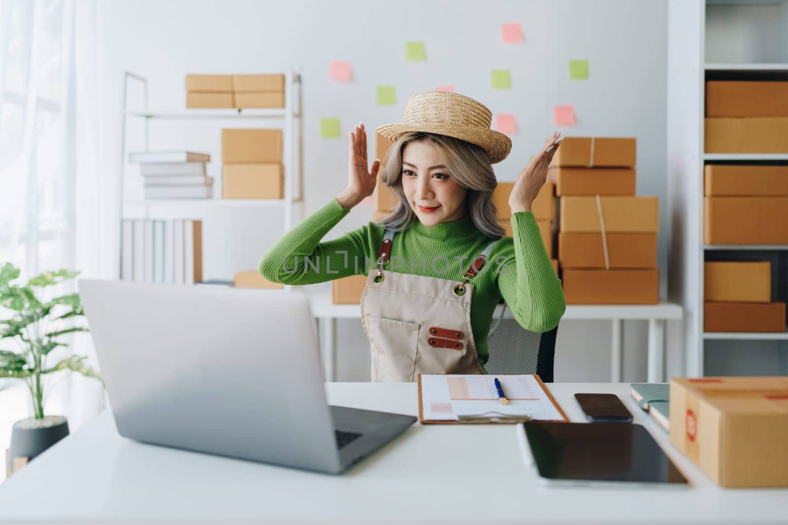 Starting small business entrepreneur of independent Asian female online seller talking on computer to video with a customer and packing products for delivery to the customer. SME delivery concept by Manastrong