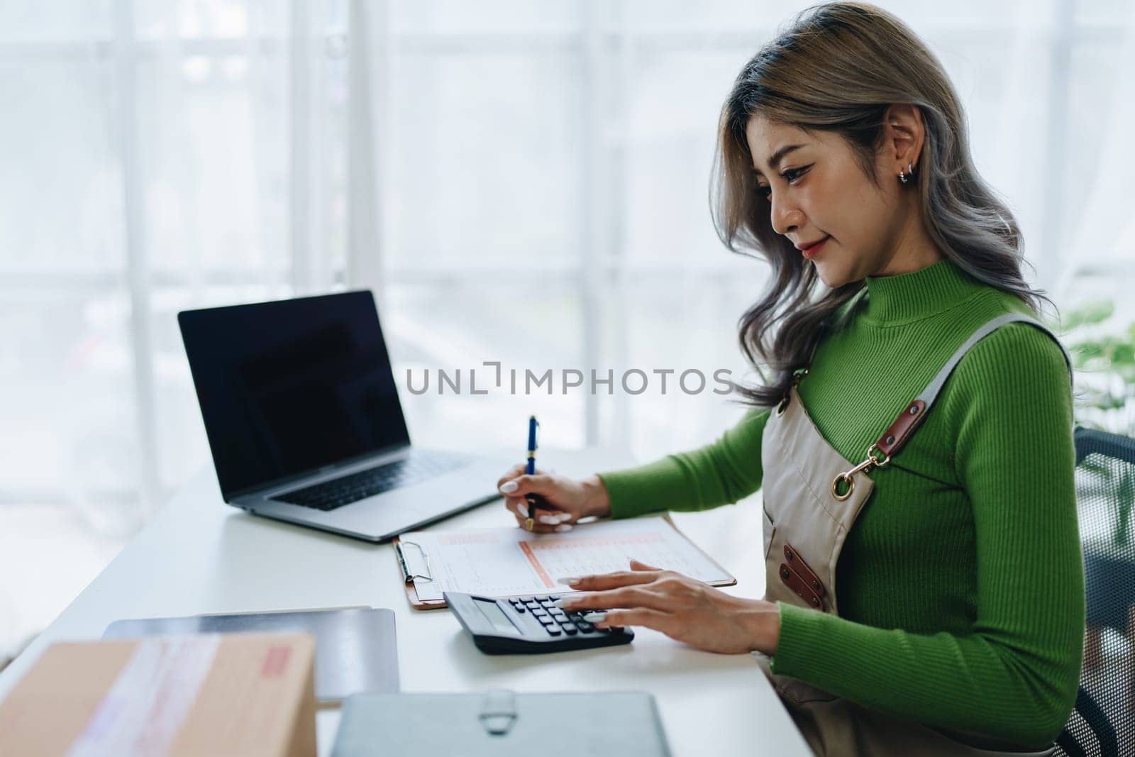 Small business, online business owner, young woman is using profit calculator and checking inventory.
