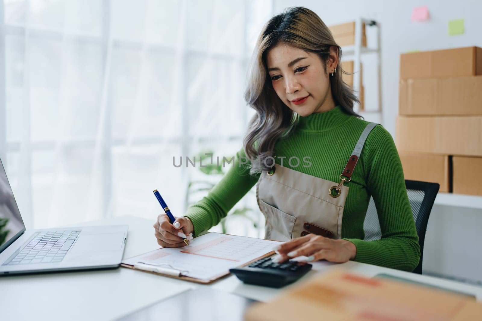 Small business, online business owner, young woman is using profit calculator and checking inventory.