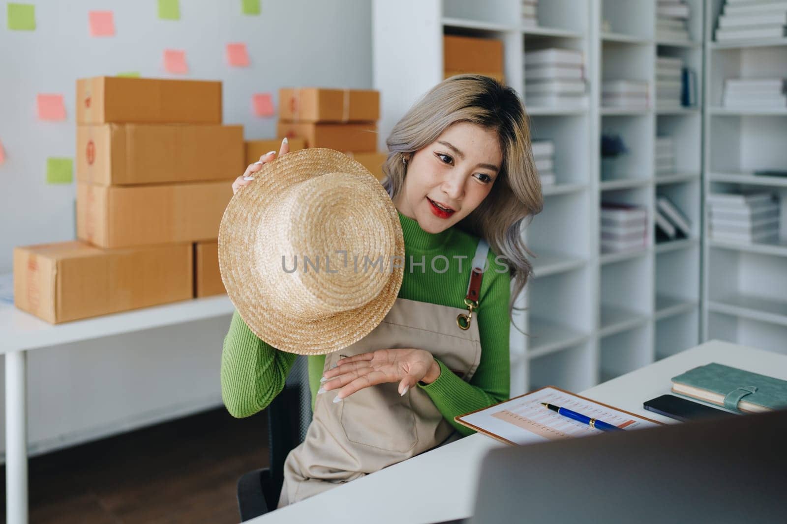 Starting small business entrepreneur of independent Asian female online seller talking on computer to video with a customer and packing products for delivery to the customer. SME delivery concept by Manastrong