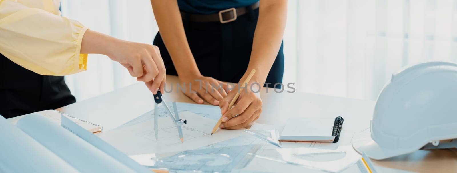 Professional architect team used divider measure during draft blueprint on table with architectural document, safety helmet and blueprint scatter around. Closeup. Focus on hand. Delineation.