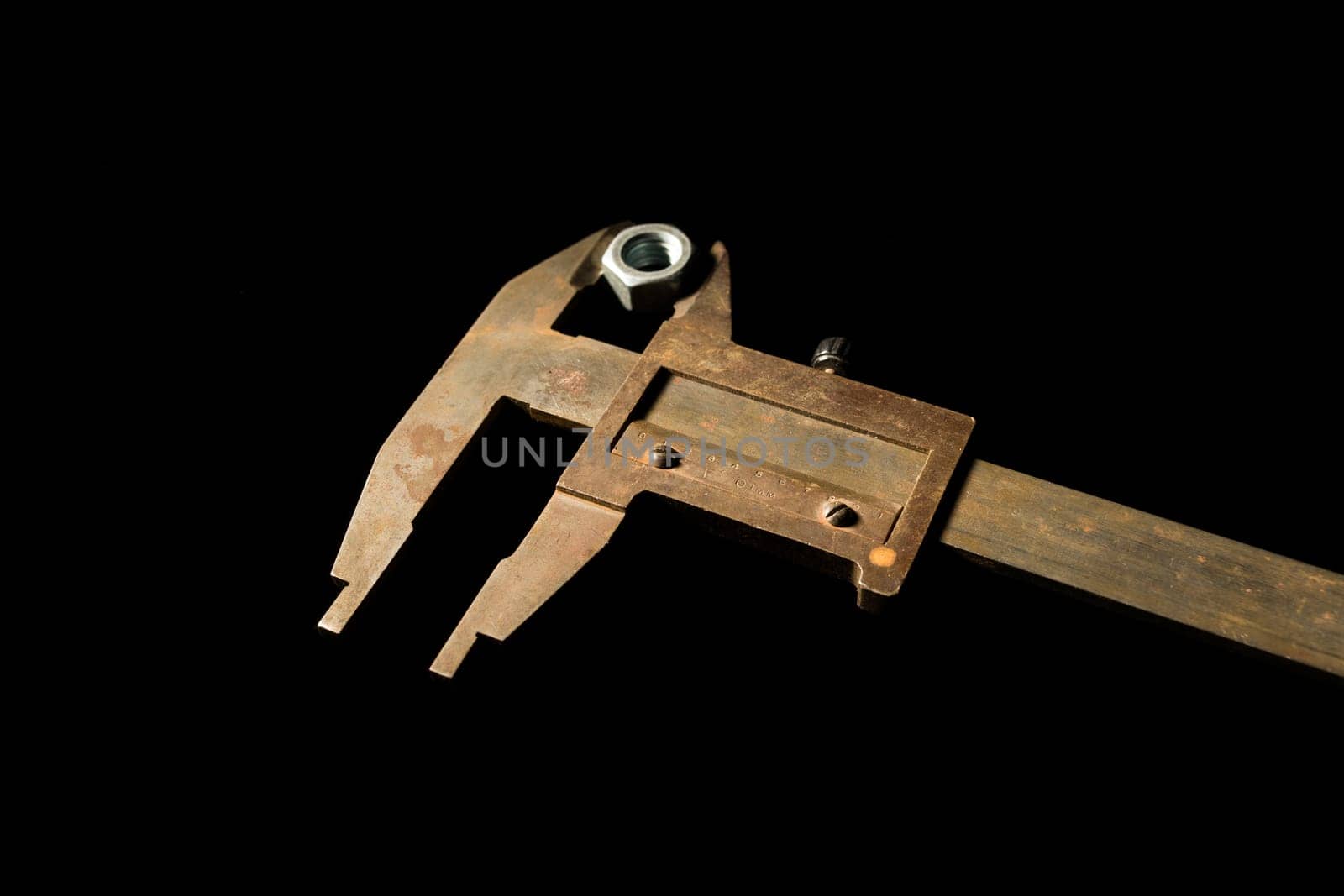 Old tools caliper with screw-nut in front of a black background - image