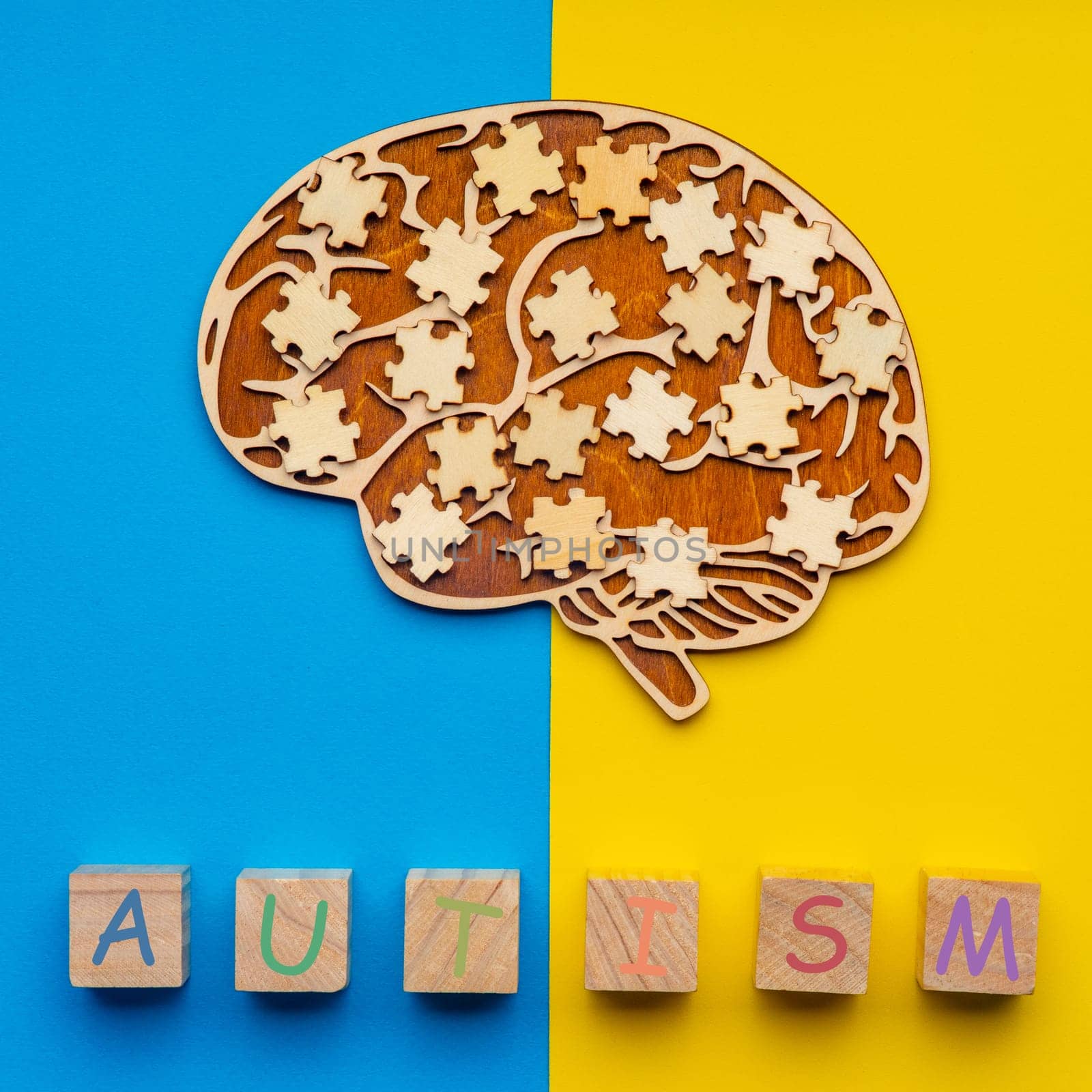 Mock up of a human brain with scattered puzzle pieces on a yellow and blue background. Six cubes with the inscription autism.