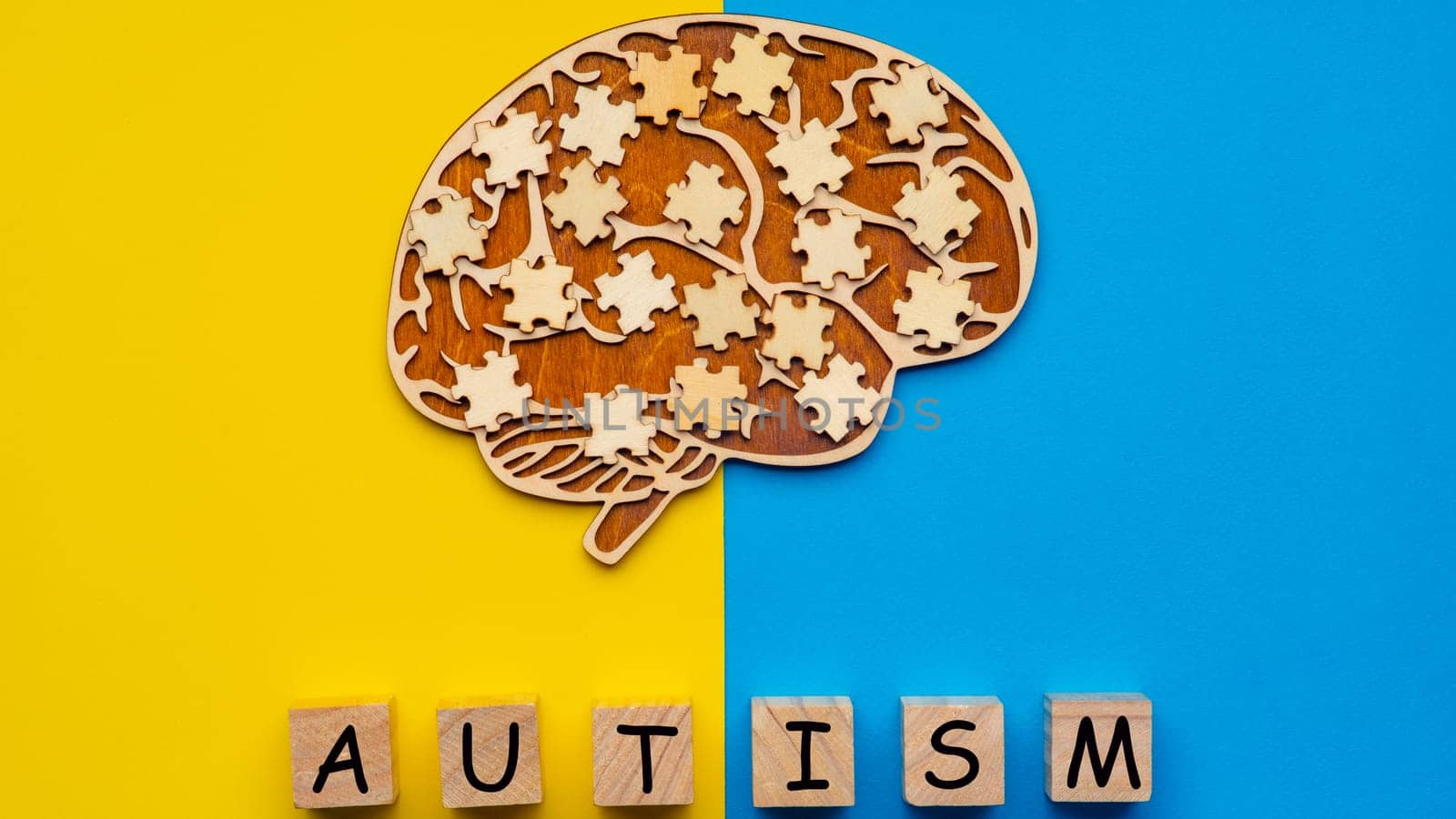 Mock up of a human brain with scattered puzzle pieces on a yellow and blue background. Six cubes with the inscription autism.