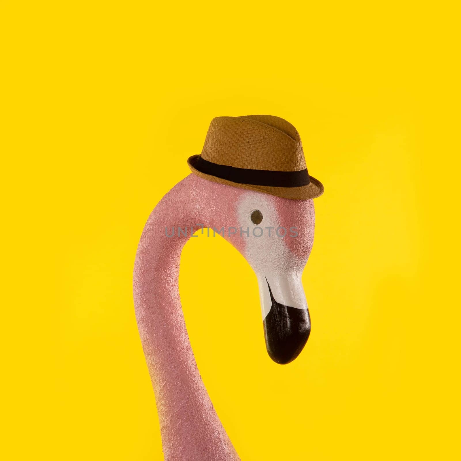 Decorative figure of pink flamingo in a straw hat on yellow background