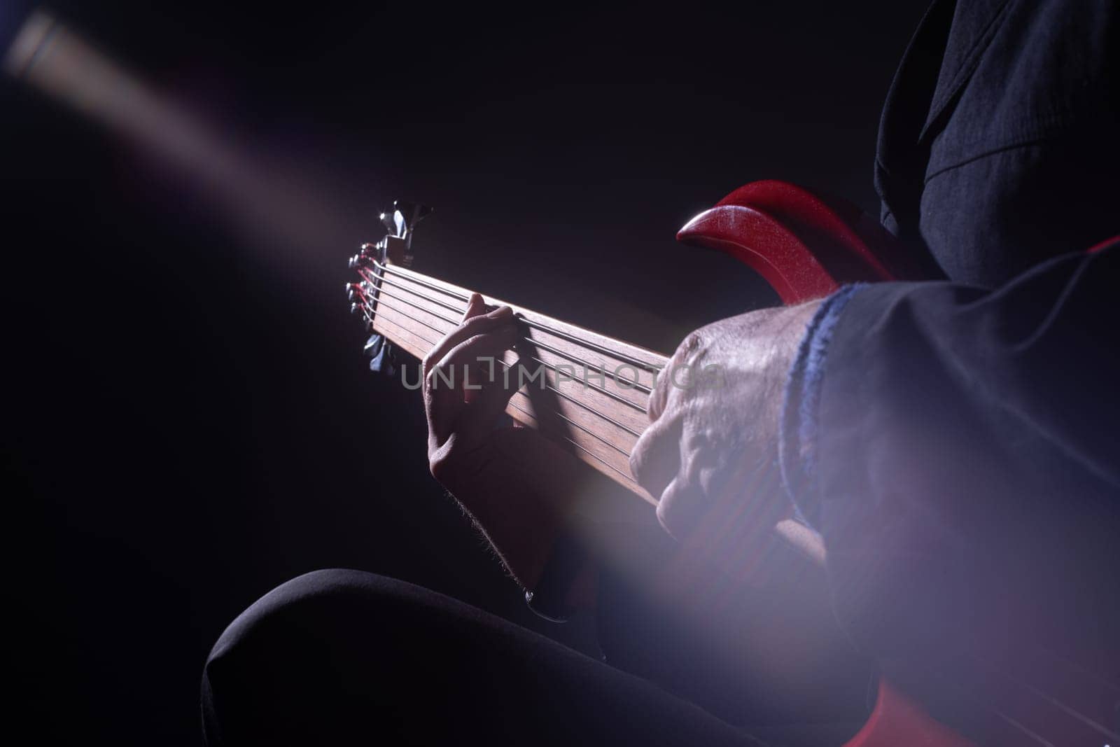 Male musician playing six-string fretless bass guitar on dark background