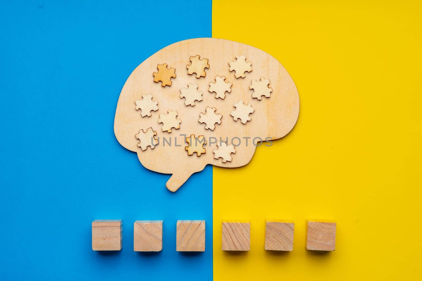 Mock up of a human brain with scattered puzzle pieces on a yellow and blue background. Six cubes in which you can write the word autism in your font.