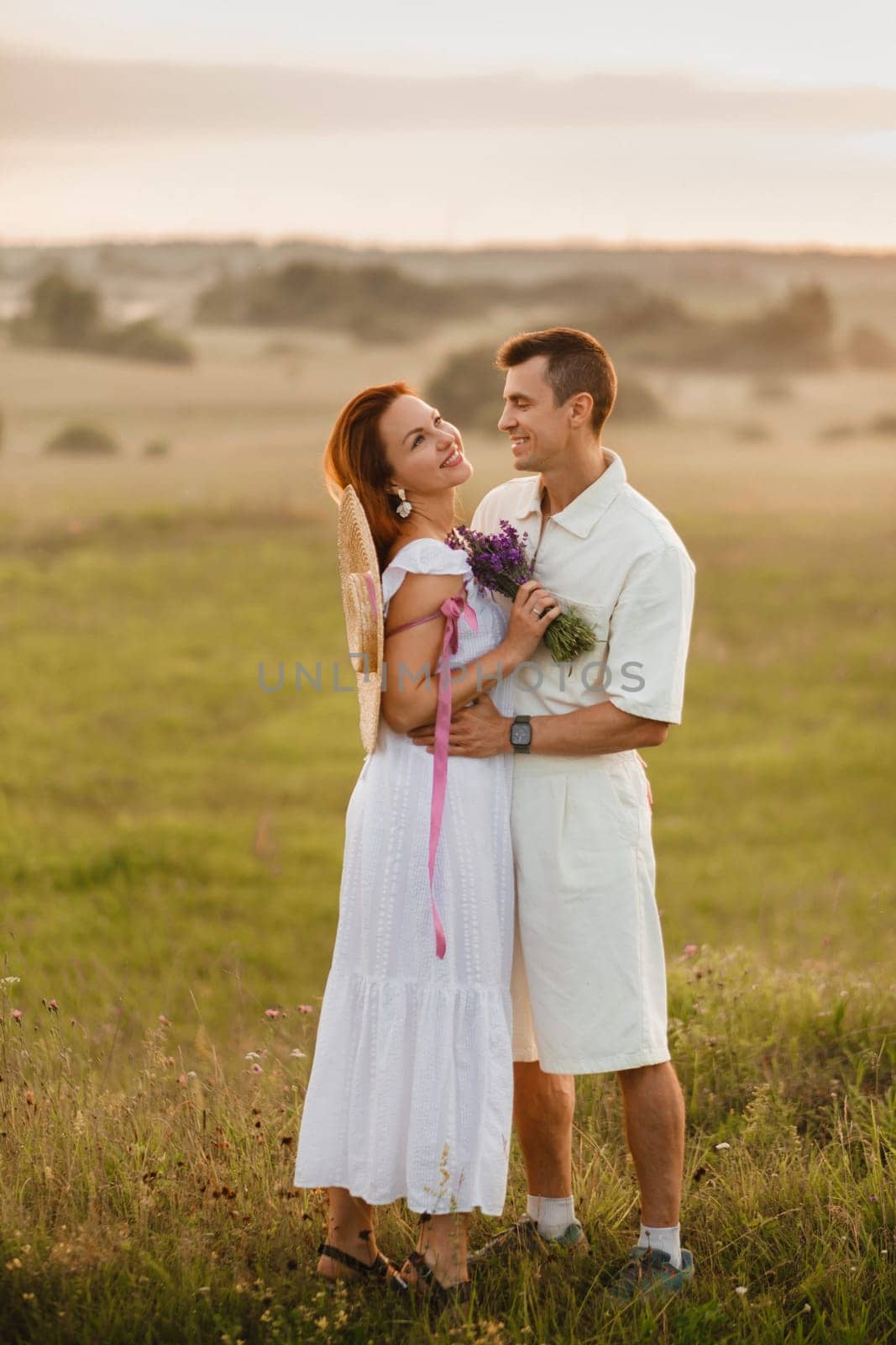 A couple in love in white clothes in a field at a red sunset.