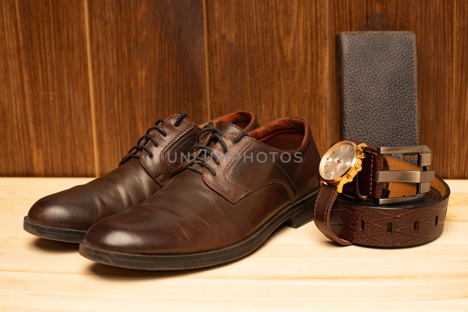 Men's accessories with brown leather wallet, belt, shoes and watch on wooden background