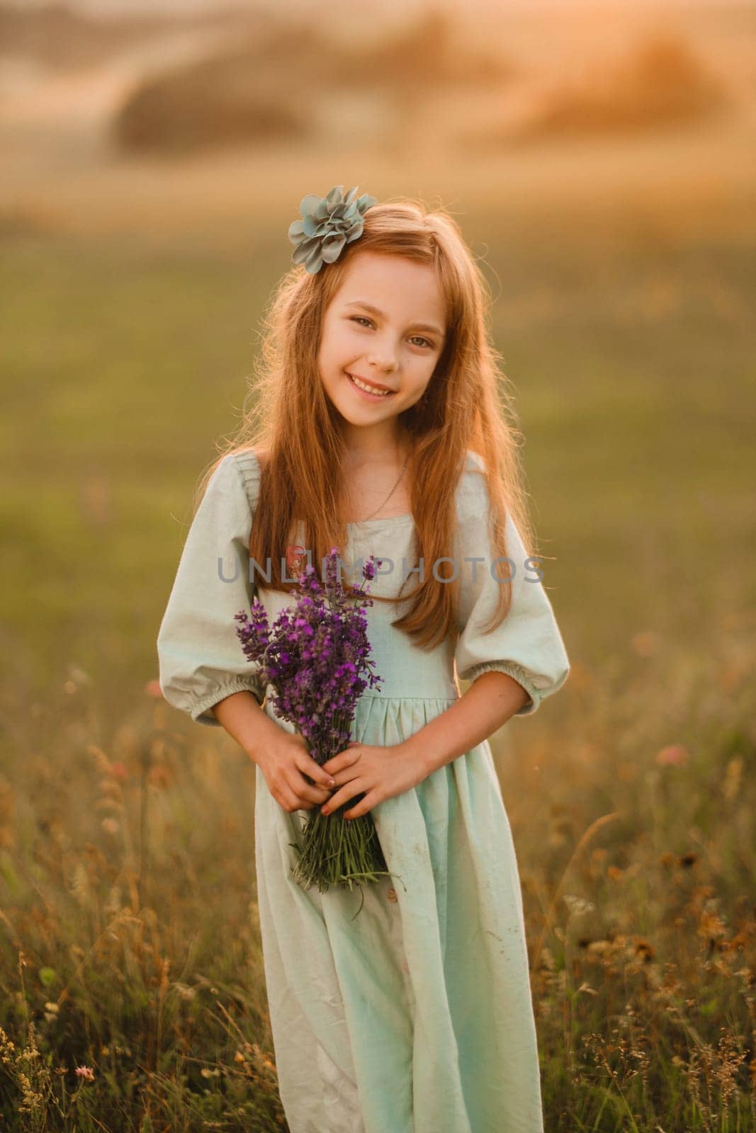 a little girl in a light green dress with a bouquet of lavender in a field at sunset.