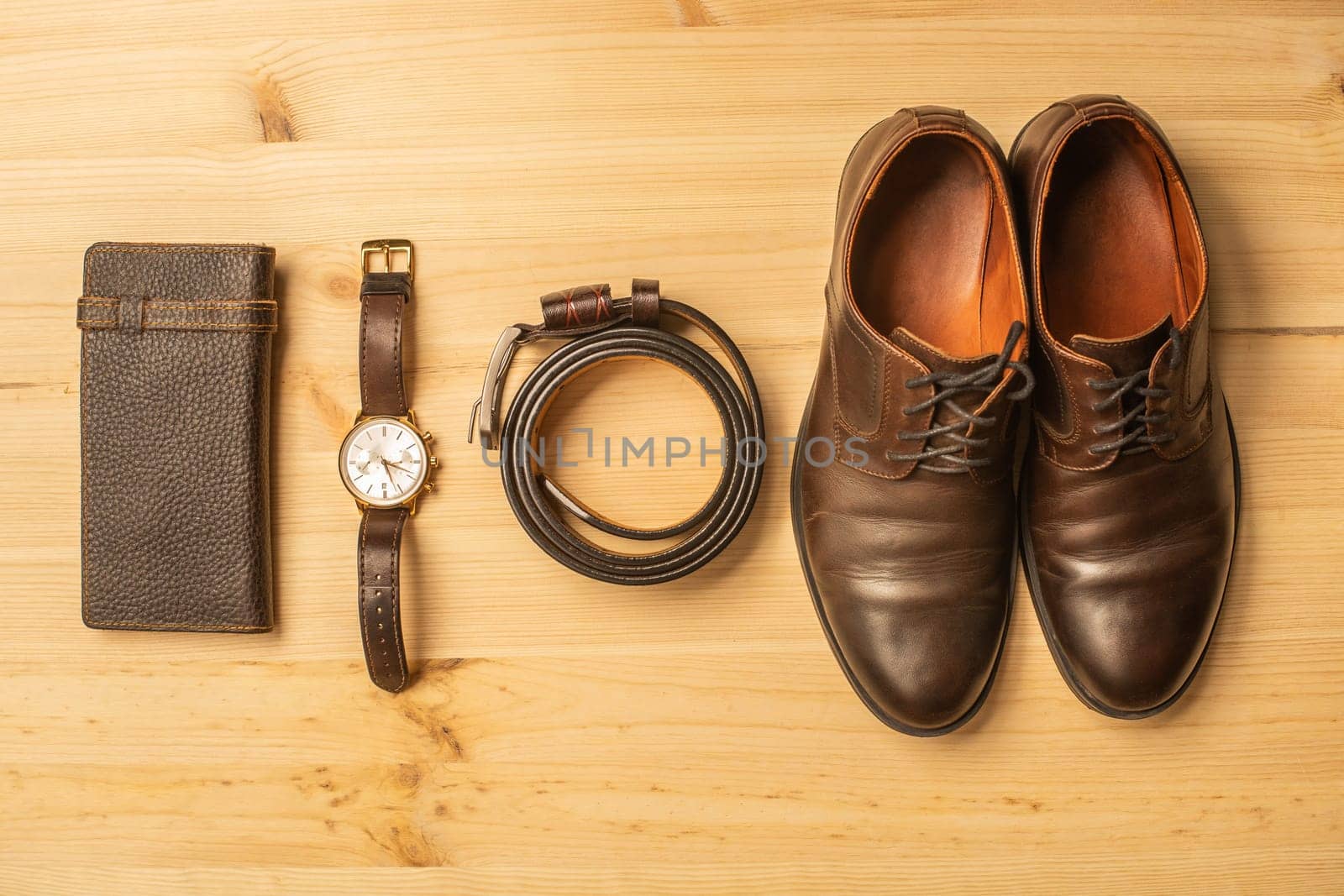 Men's accessories with brown leather wallet, belt, shoes and watch on wooden background