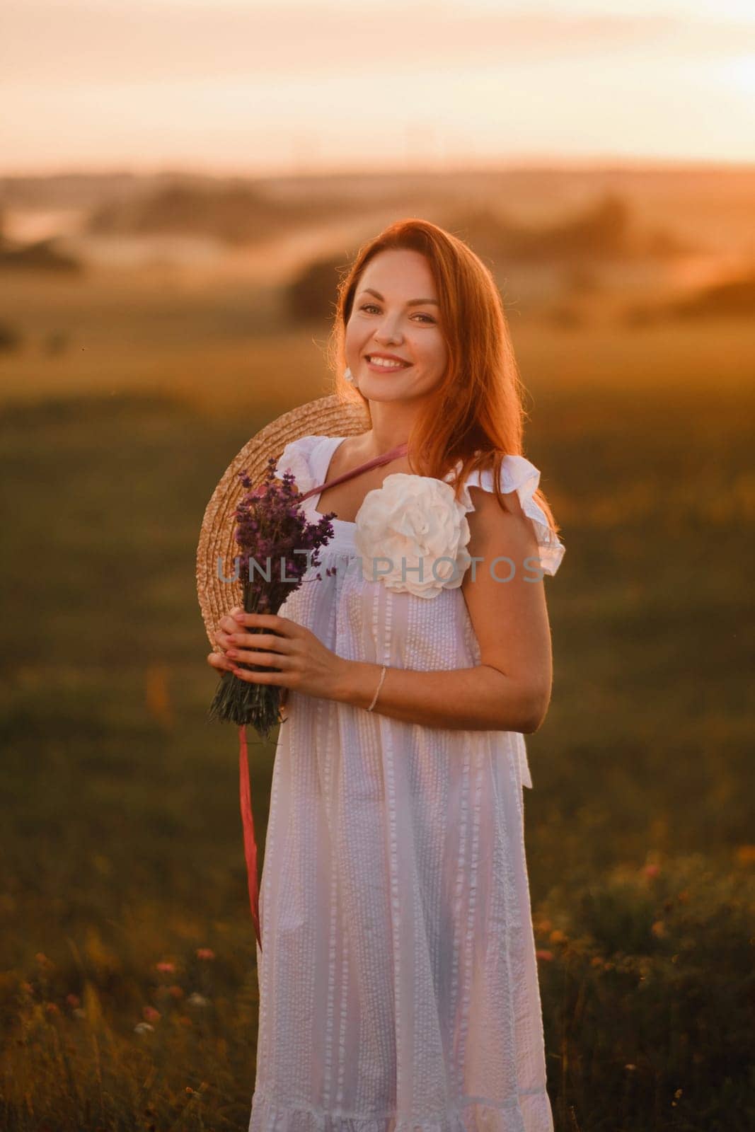 A girl in a white dress with a bouquet of lavender flowers stands in a field at sunset by Lobachad