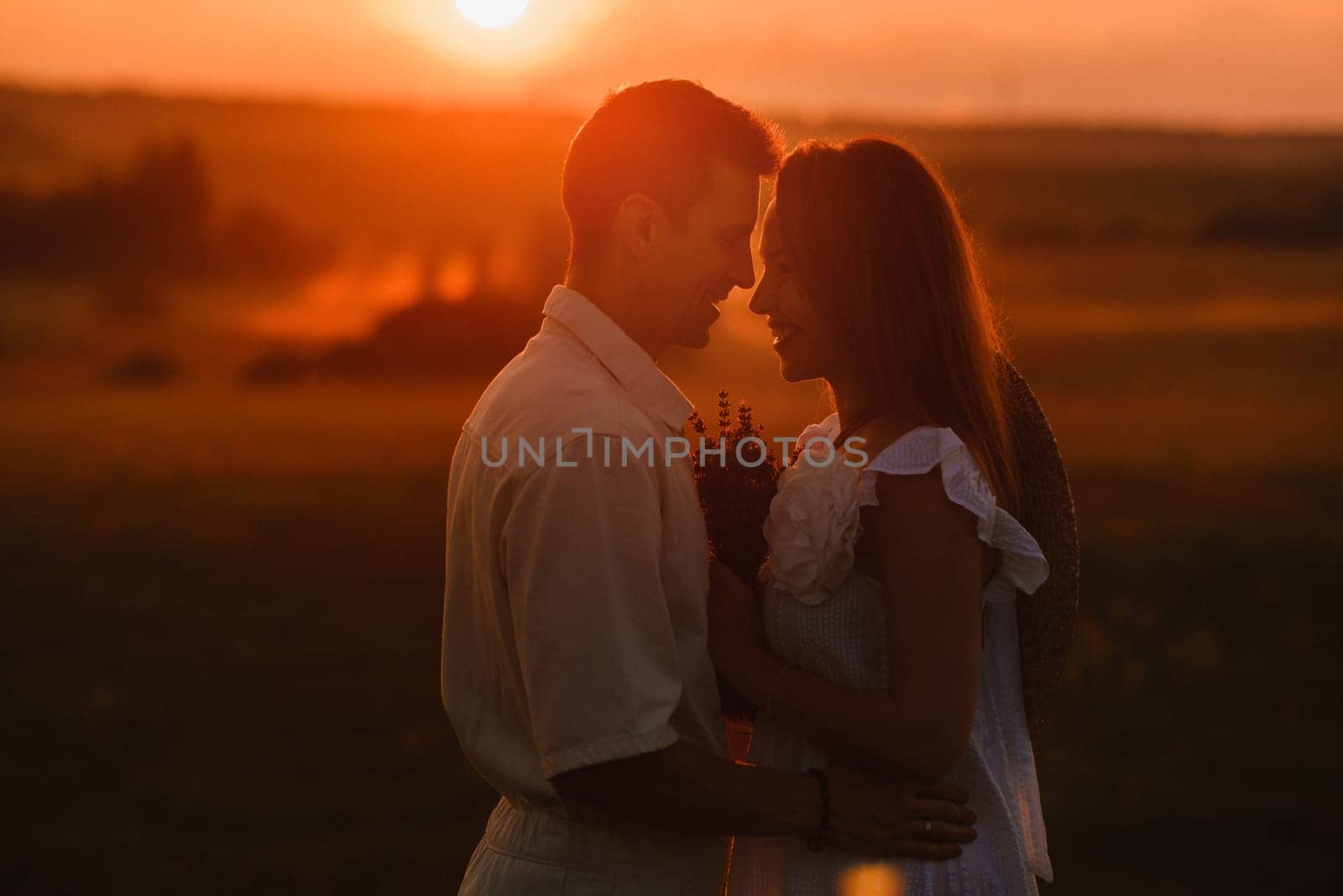 A couple in love in white clothes in a field at a red sunset by Lobachad