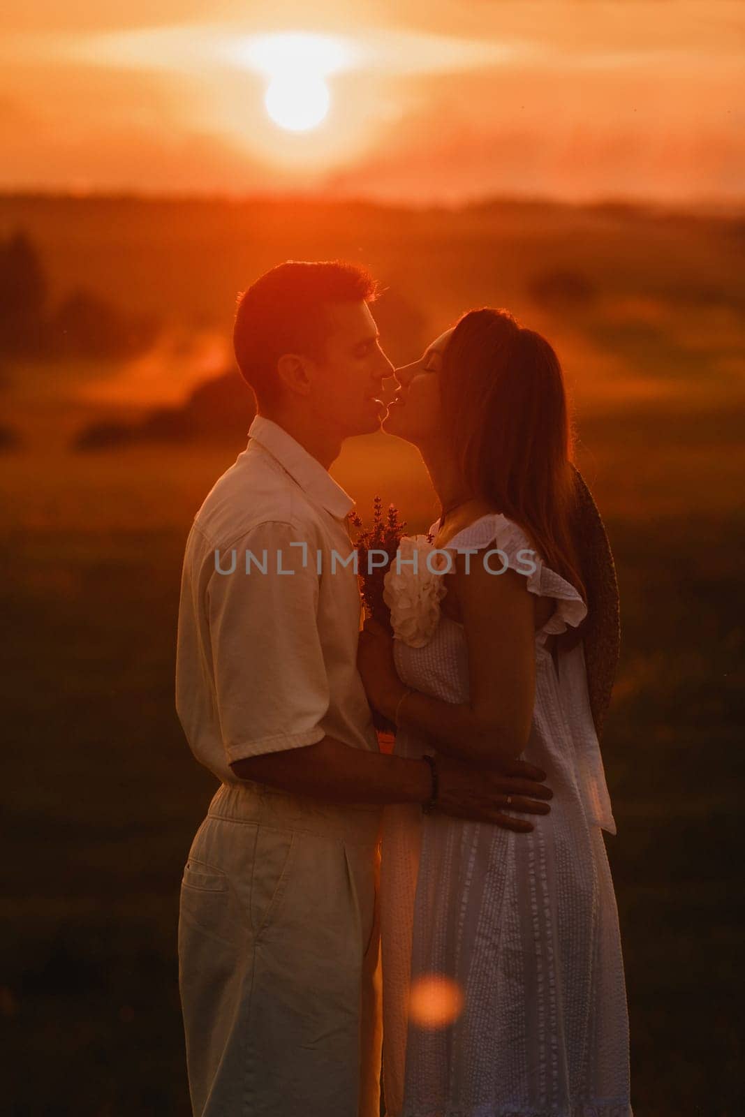 A couple in love in white clothes in a field at a red sunset.