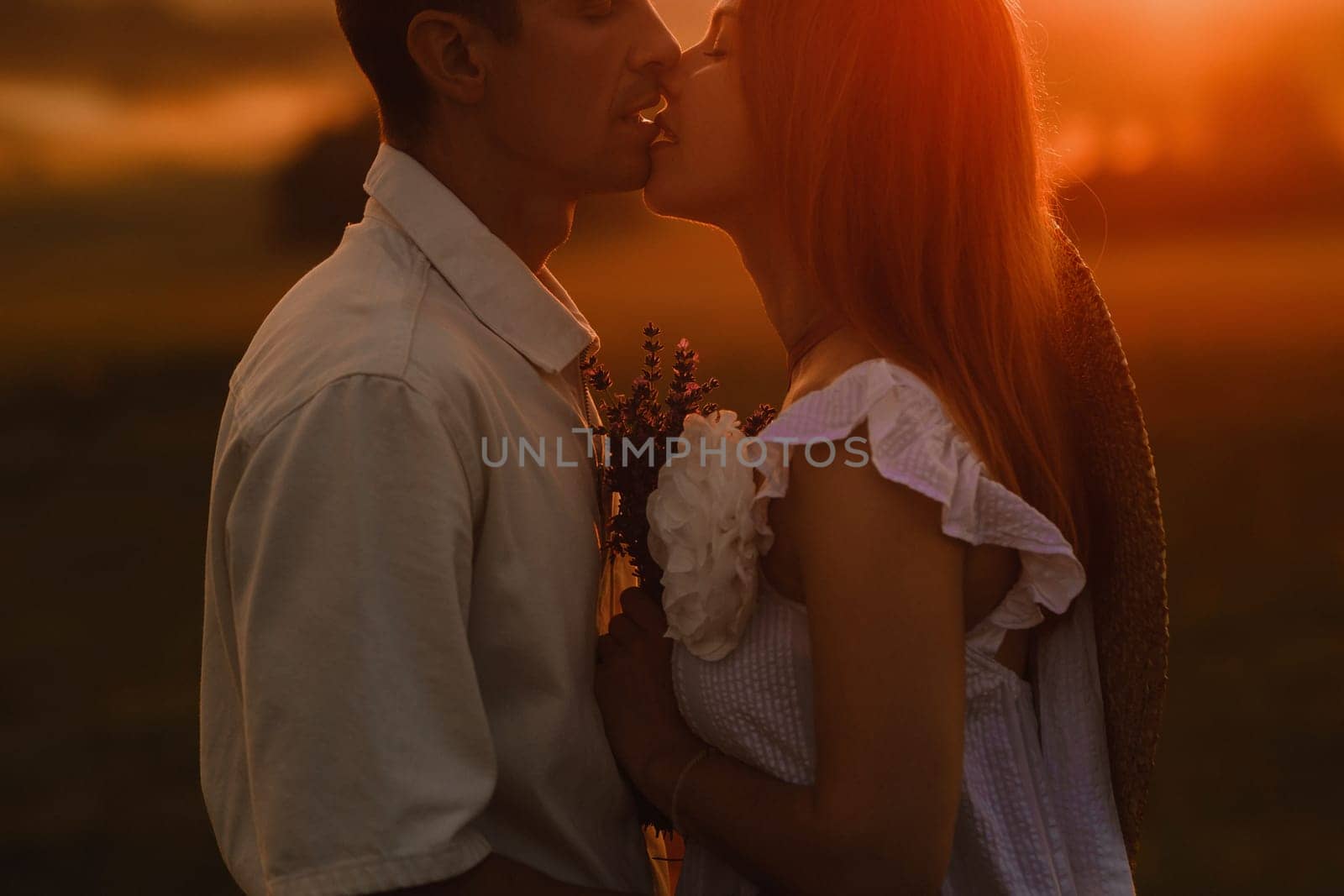 A couple in love in white clothes in a field at a red sunset.