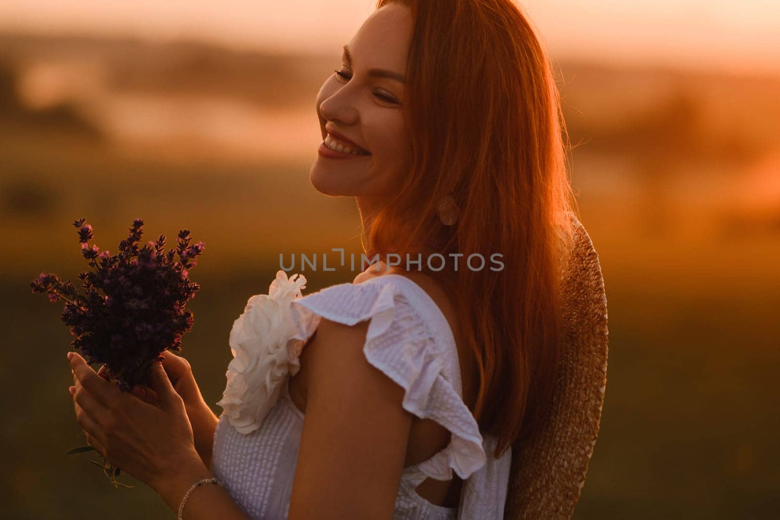 A girl in a white dress with a bouquet of lavender flowers stands in a field at sunset by Lobachad