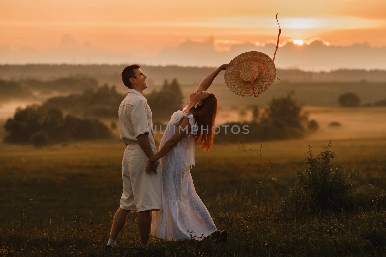 A couple in love in white clothes in a field at a red sunset.