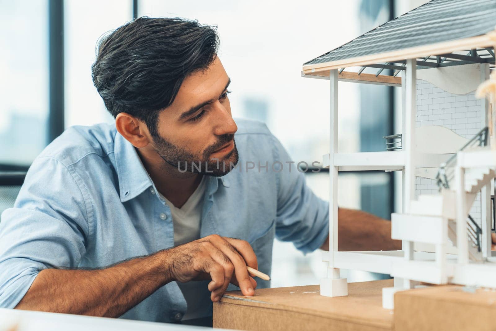 Closeup portrait of smart caucasian architect engineer inspect house model while thinking about building construction at architect studio on table with project plan, blueprint, equipment. Tracery.