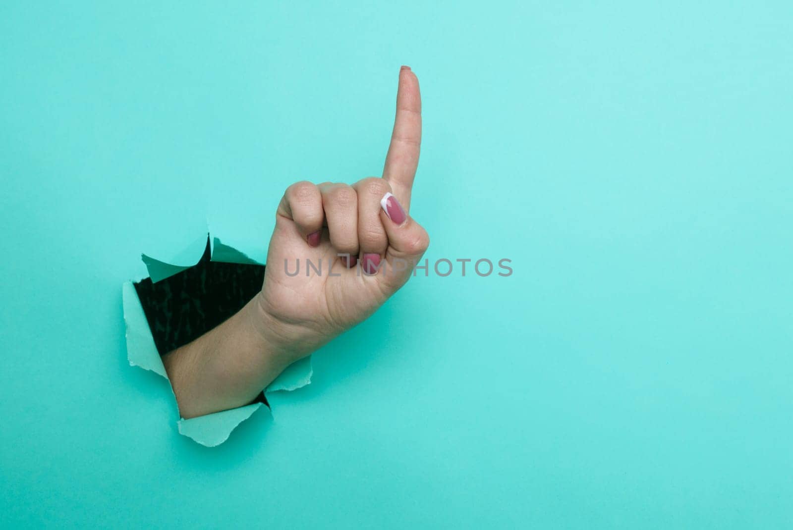 Female hand pointing finger up close-up. Copy space. Torn paper, blue background.