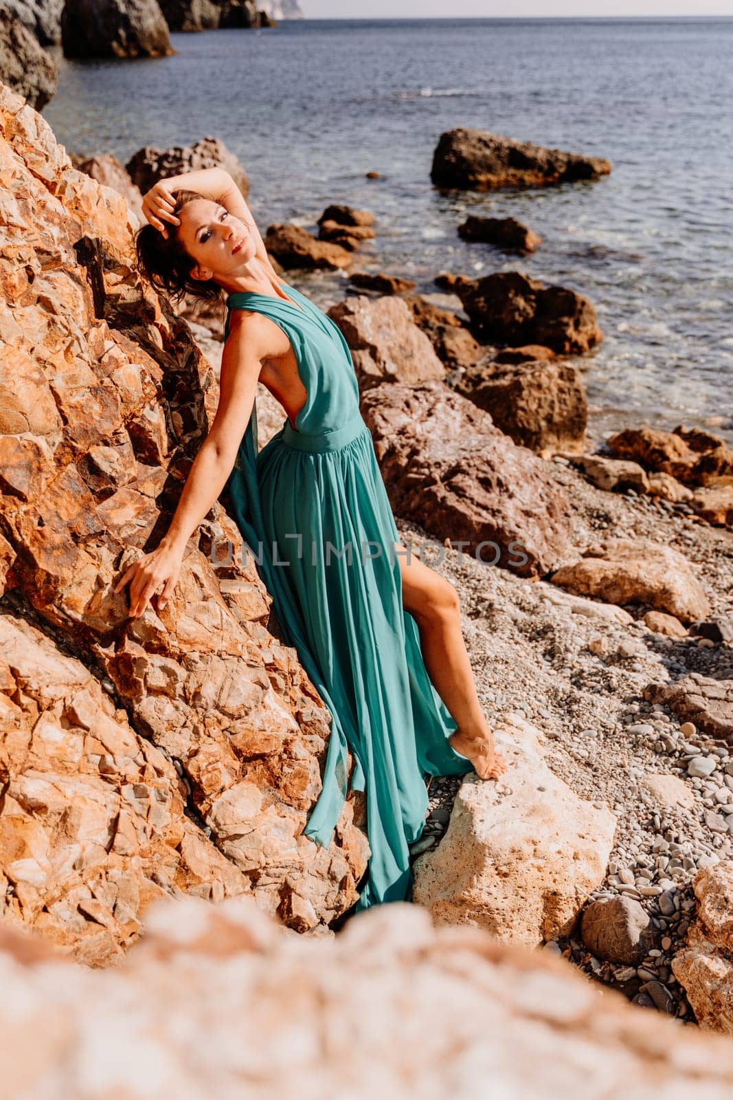 Woman green dress sea. Woman in a long mint dress posing on a beach with rocks on sunny day. Girl on the nature on blue sky background