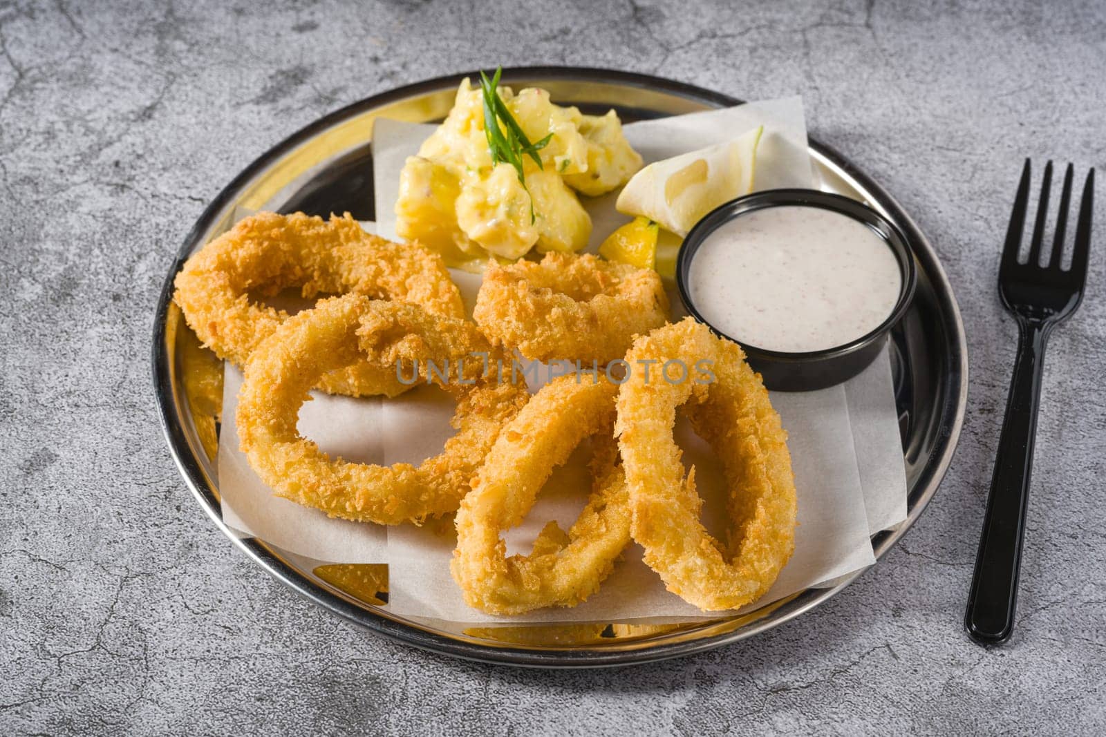 Fried calamari with potato salad next to it on stone table